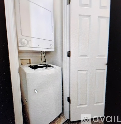 A white washing machine is in a small space next to a white door.