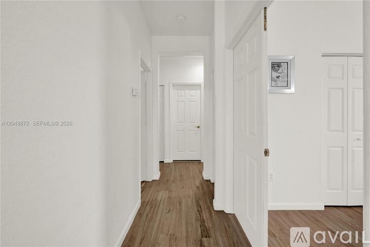 A hallway with white walls and wooden floors leading to a door.