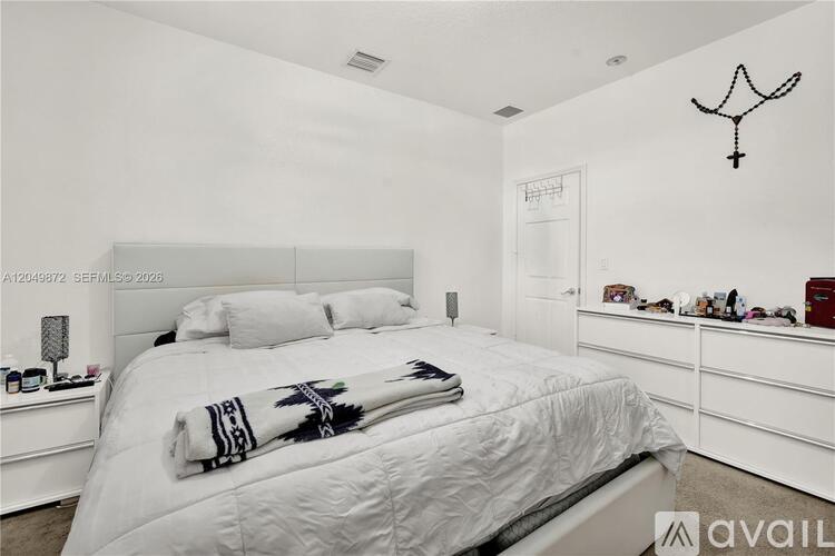 A bedroom with a large bed and a white wall with a black design hanging on it.
