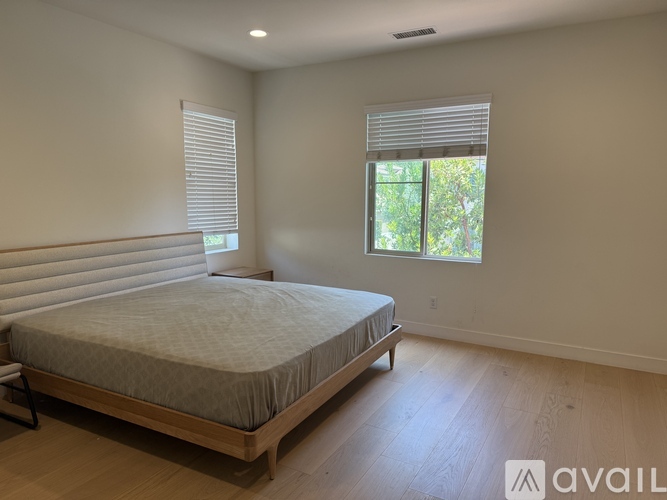 A bedroom with a large bed and a window with blinds.