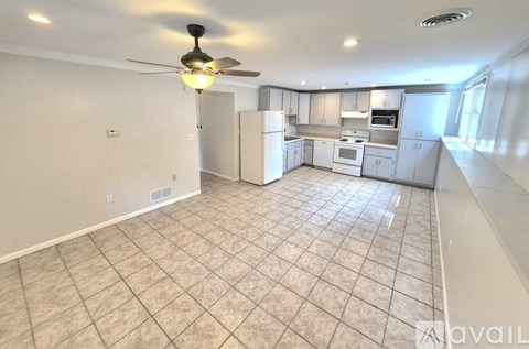 A kitchen with white cabinets and appliances, a ceiling fan, and a tiled floor.