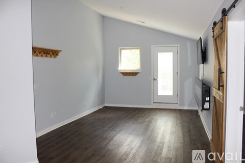 A room with wooden floors and white walls, with a window and a door visible.