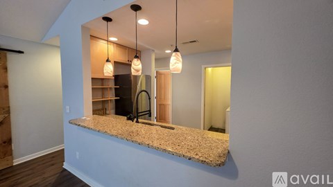 A modern kitchen with a granite countertop and pendant lights.
