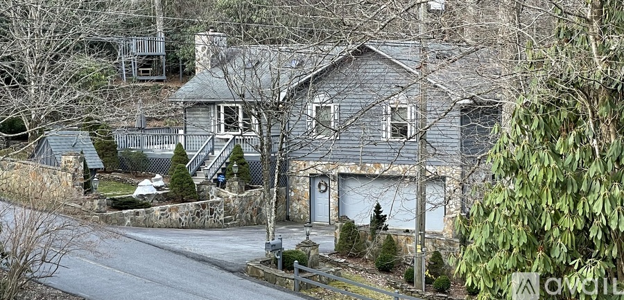 A house with a grey exterior is surrounded by trees and a driveway.
