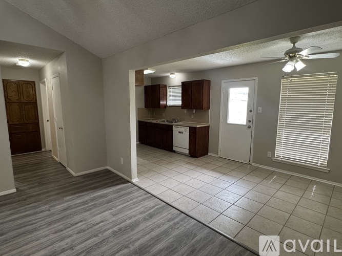 A living room with a kitchen in the background and a fan on the ceiling.