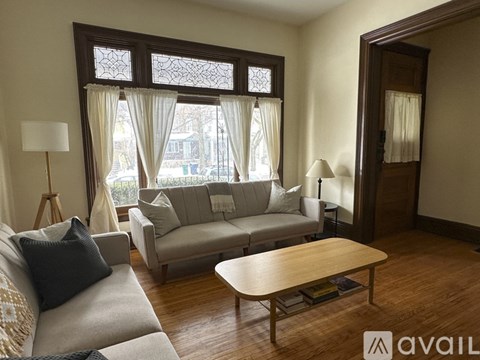 A living room with a grey couch, a wooden coffee table, and a large window with curtains.