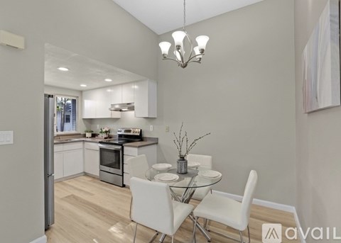 A modern kitchen with white chairs and a glass table.