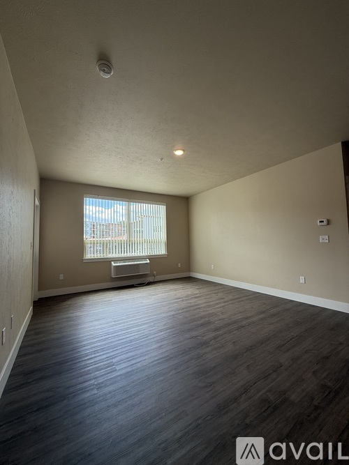A spacious room with wooden flooring and a window with blinds.