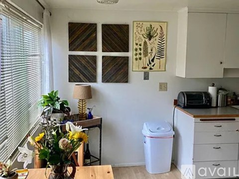 A white trash can sits in a kitchen next to a table with a vase of flowers on it.
