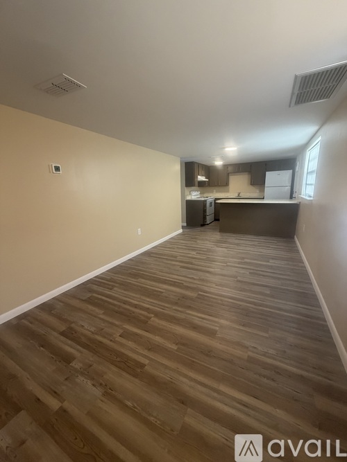 A room with wooden flooring and a kitchen area in the background.