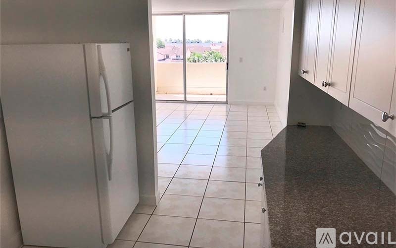 A kitchen with a refrigerator, cabinets, and a view of the backyard through the window.