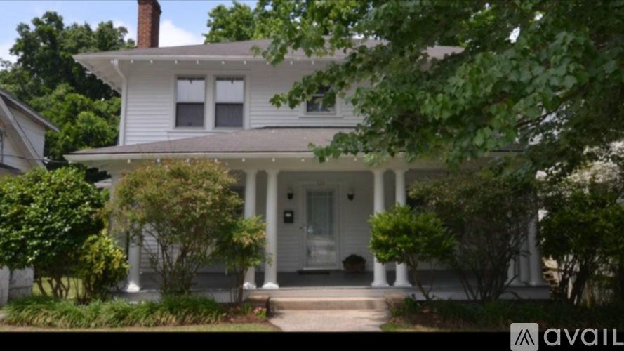 A white house with a porch and a tree in front.