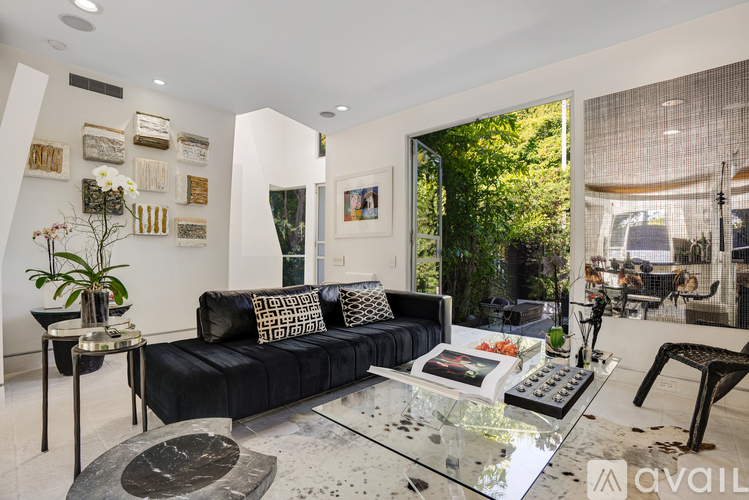 A black couch with pillows sits in a living room with a glass table in front of it.