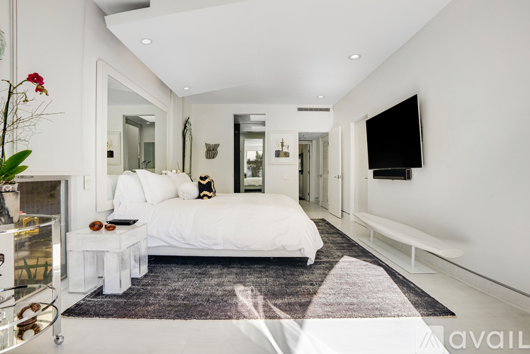 A white bedroom with a large bed and a flat screen TV mounted on the wall.