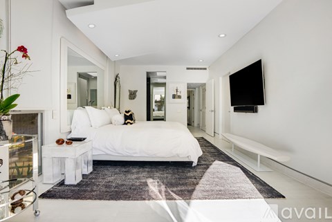 A white bedroom with a large bed and a flat screen TV mounted on the wall.