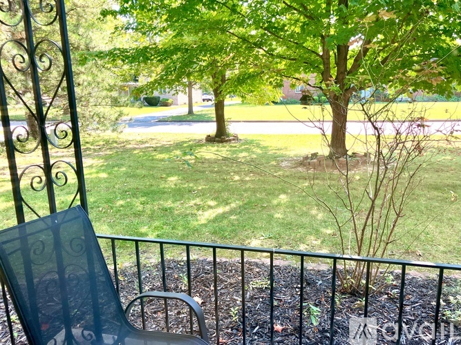 A black metal chair is on a balcony with a view of a green lawn and trees.