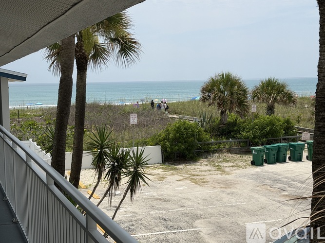 A view from a balcony overlooking a beach with palm trees and a few people in the distance.