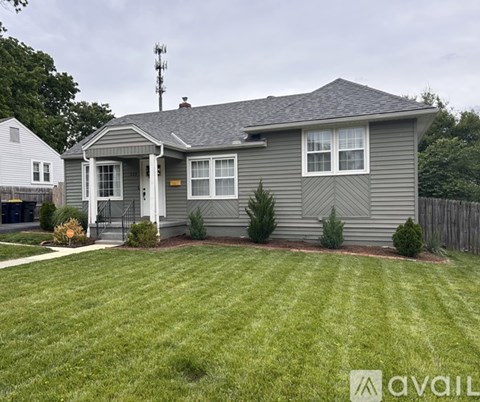 A house with a grey exterior and a white door is surrounded by a green lawn.