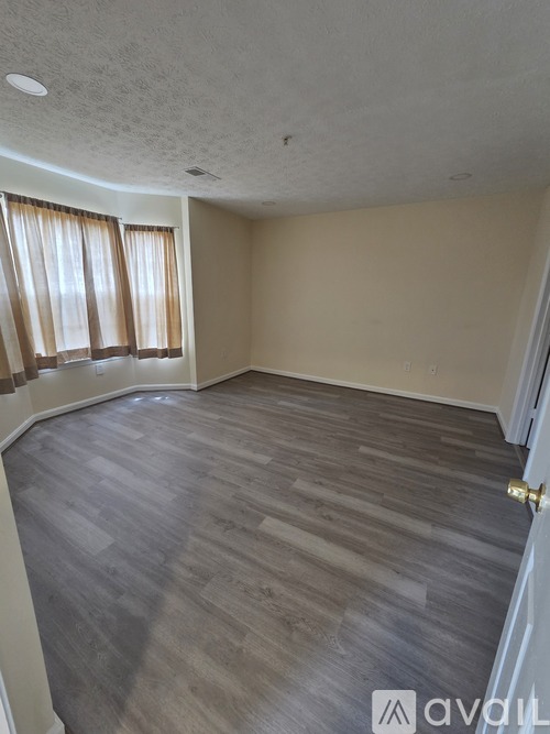 A room with wooden flooring and a window with curtains.