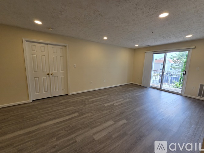 A spacious room with wooden flooring and a sliding glass door leading to a balcony.