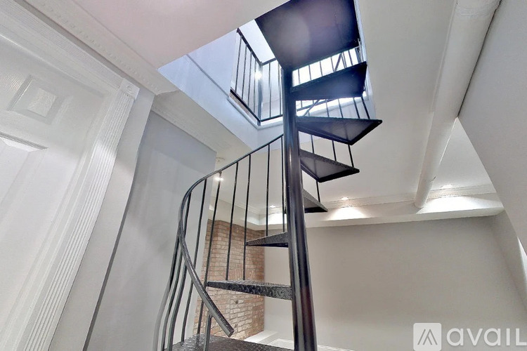 A spiral staircase with a metal railing and a skylight above it.