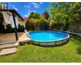 A small above ground pool surrounded by a wooden deck and a green lawn.