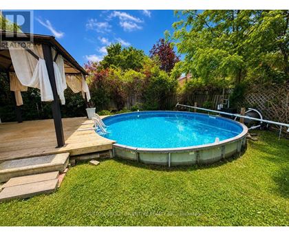 A small above ground pool surrounded by a wooden deck and a green lawn.