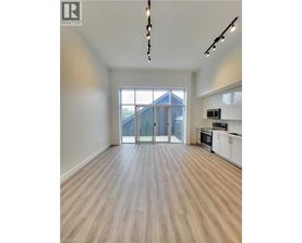 A spacious room with wooden flooring and a kitchen area with white cabinets.