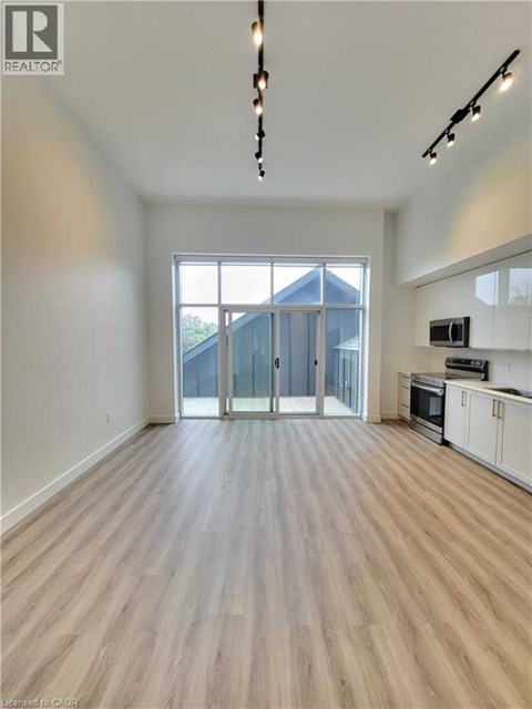 A spacious room with wooden flooring and a kitchen area with white cabinets.
