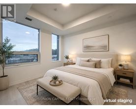 A bedroom with a large bed, a nightstand, and a window overlooking a cityscape.