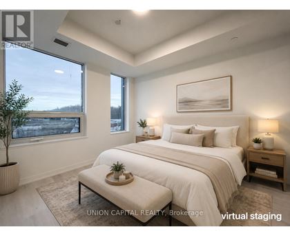 A bedroom with a large bed, a nightstand, and a window overlooking a cityscape.
