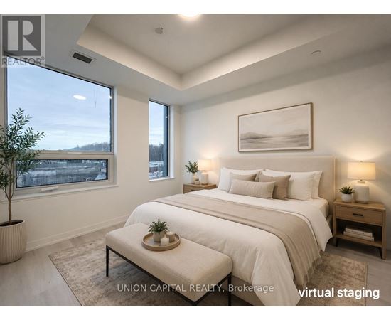 A bedroom with a large bed, a nightstand, and a window overlooking a cityscape.
