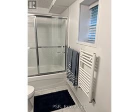 A bathroom with a toilet, a glass shower door, a towel rack, and a window.