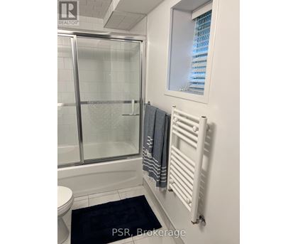 A bathroom with a toilet, a glass shower door, a towel rack, and a window.