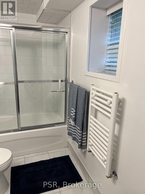 A bathroom with a toilet, a glass shower door, a towel rack, and a window.