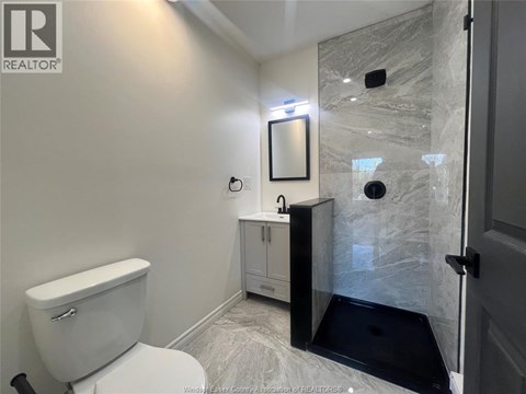 A white toilet is in a bathroom with a marble shower.