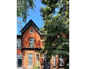 A red brick house with a black roof and a tree in front.