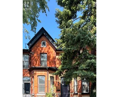 A red brick house with a black roof and a tree in front.