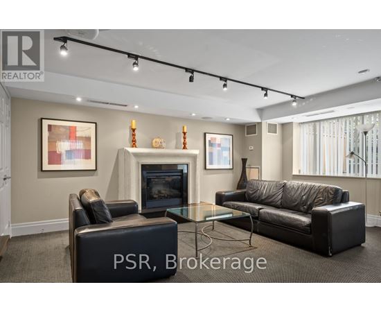 A living room with a black leather couch, a black ottoman, and a glass coffee table.