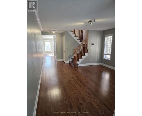 A spacious room with wooden floors and a staircase.