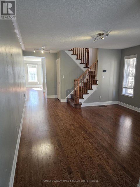 A spacious room with wooden floors and a staircase.