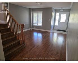 A spacious room with wooden floors and a staircase leading to the upper level.