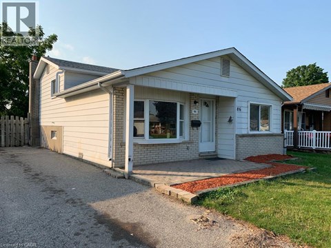 A small house with a white door and windows is surrounded by a gravel driveway.