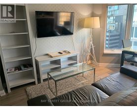 A living room with a television, a glass coffee table, and a large window.