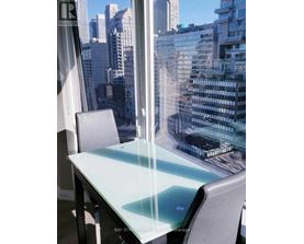 A glass table with a chair in front of a window overlooking a cityscape.