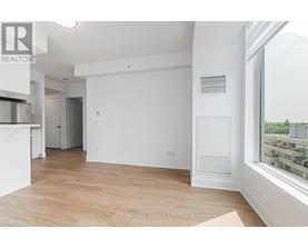 A spacious, empty room with a large window and hardwood flooring.