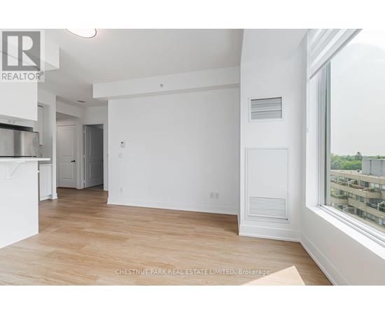 A spacious, empty room with a large window and hardwood flooring.