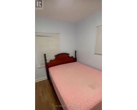 A bed with a pink cover sits in a room with white walls.