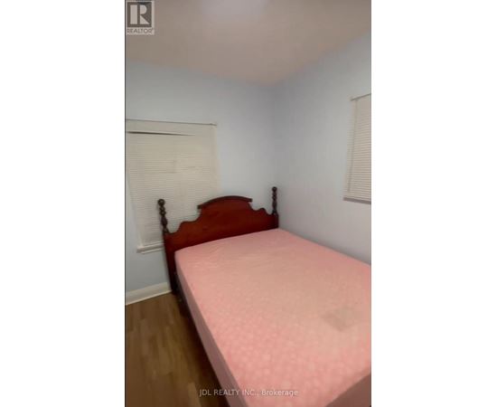 A bed with a pink cover sits in a room with white walls.