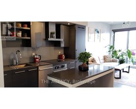 A modern kitchen with a large island and a living area with a couch and plants.